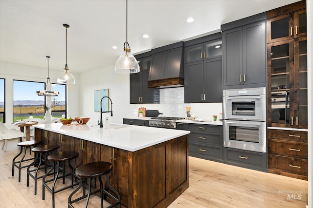 kitchen with pendant lighting, a center island with sink, sink, light hardwood / wood-style floors, and stainless steel double oven