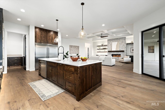 kitchen with a stone fireplace, light hardwood / wood-style flooring, an island with sink, and coffered ceiling