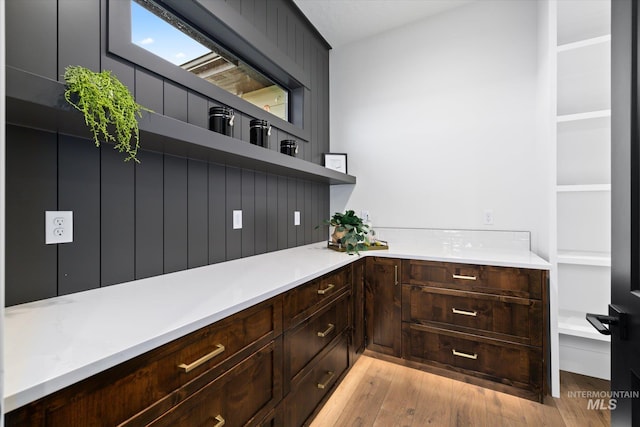 bar with dark brown cabinets and light wood-type flooring