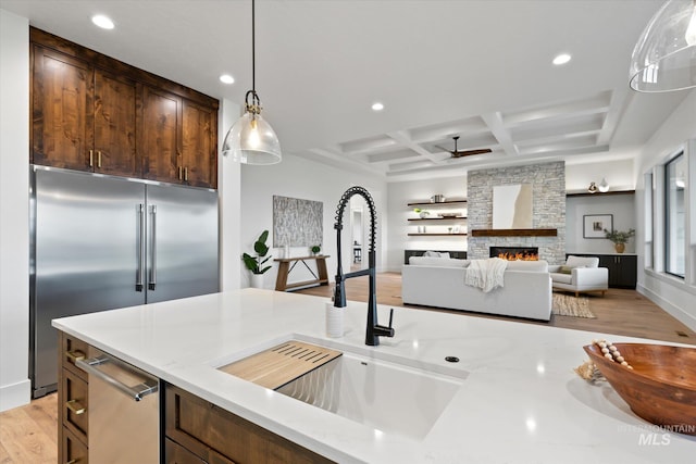 kitchen with coffered ceiling, decorative light fixtures, a fireplace, appliances with stainless steel finishes, and light wood-type flooring