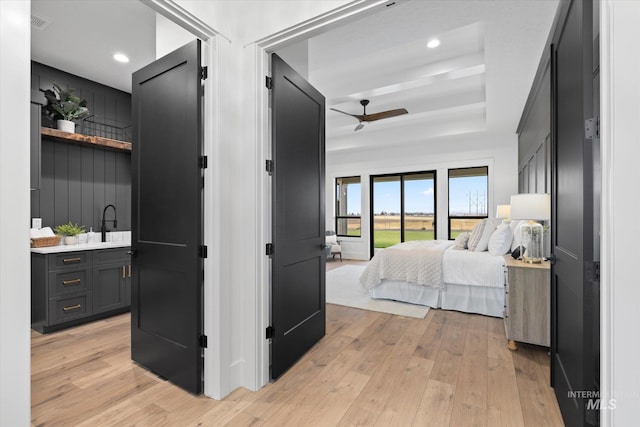 bedroom with ceiling fan, a raised ceiling, sink, and light hardwood / wood-style flooring