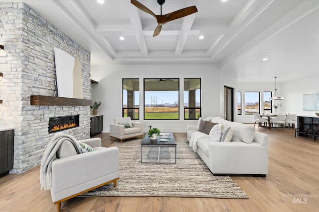 living room featuring coffered ceiling, ceiling fan, beamed ceiling, a fireplace, and light hardwood / wood-style floors