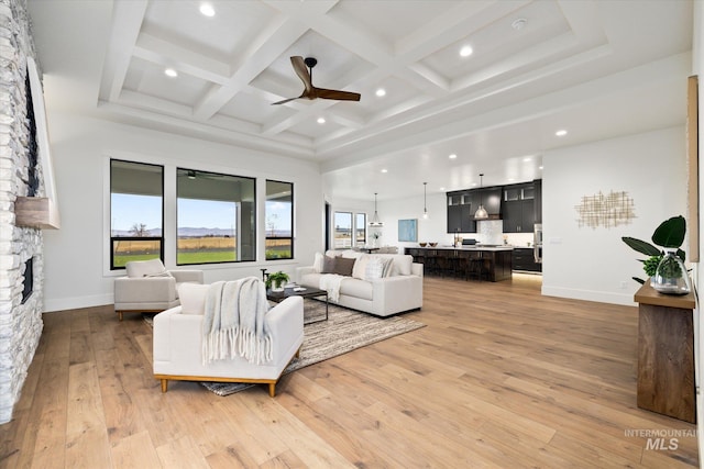 living room featuring a stone fireplace, ceiling fan, light hardwood / wood-style flooring, and beamed ceiling