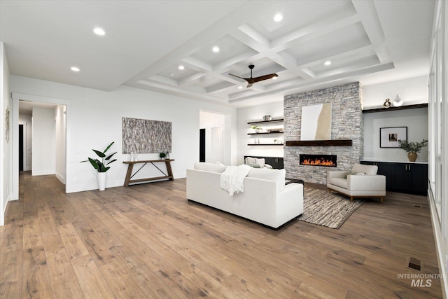 living room with hardwood / wood-style floors, a stone fireplace, beamed ceiling, and coffered ceiling