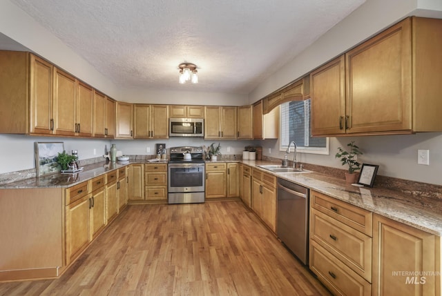 kitchen with sink, stone counters, stainless steel appliances, a textured ceiling, and light wood-type flooring