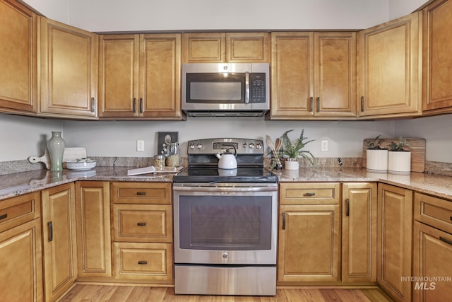 kitchen with stainless steel appliances, light stone countertops, and light wood-type flooring