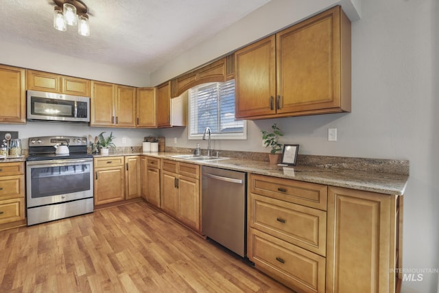 kitchen featuring sink, light stone counters, a textured ceiling, light wood-type flooring, and stainless steel appliances