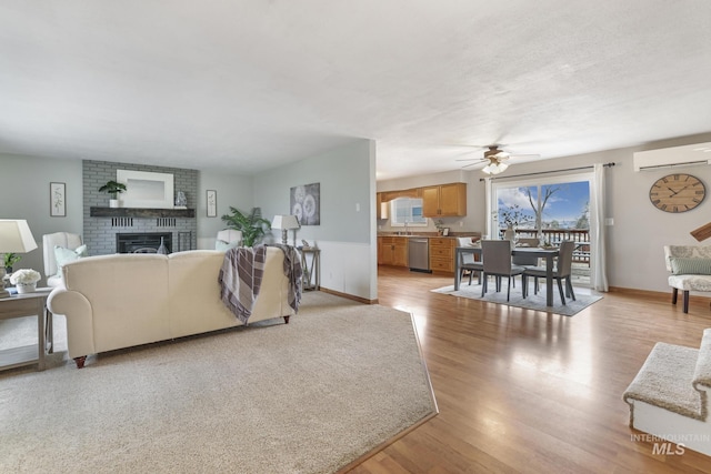 living room featuring sink, an AC wall unit, ceiling fan, a fireplace, and light hardwood / wood-style floors