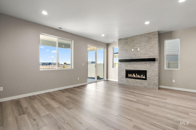 unfurnished living room featuring a stone fireplace, recessed lighting, baseboards, and wood finished floors