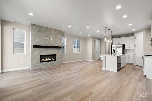 kitchen with light wood finished floors, open floor plan, a center island with sink, light countertops, and stainless steel refrigerator with ice dispenser