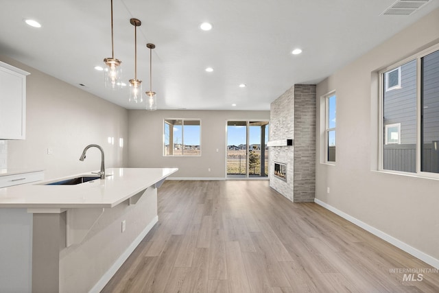 kitchen featuring visible vents, a large fireplace, light countertops, light wood-style floors, and a sink