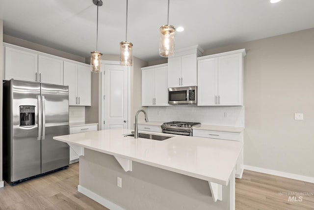 kitchen with light wood-type flooring, a sink, stainless steel appliances, decorative backsplash, and baseboards