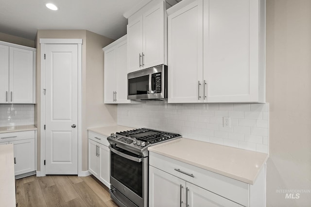 kitchen with appliances with stainless steel finishes, white cabinetry, light wood-type flooring, and light countertops