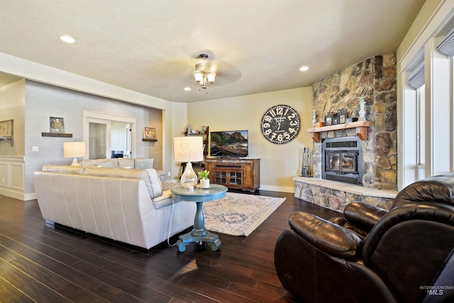 living room featuring baseboards, dark wood-style flooring, a textured ceiling, a stone fireplace, and recessed lighting