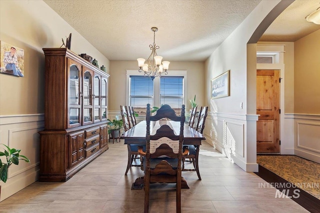 dining space featuring arched walkways, wainscoting, a textured ceiling, and an inviting chandelier