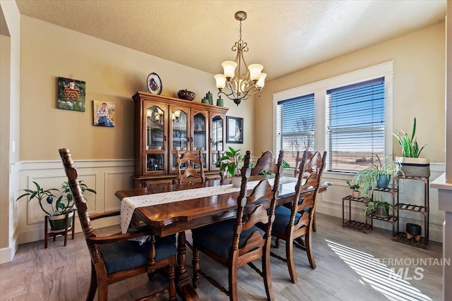 dining room featuring a wainscoted wall, a decorative wall, a textured ceiling, and an inviting chandelier