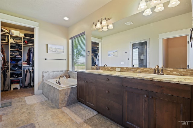 full bathroom with double vanity, a spacious closet, a sink, and a bath