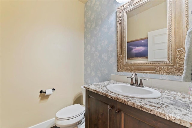 bathroom with baseboards, vanity, toilet, and wallpapered walls