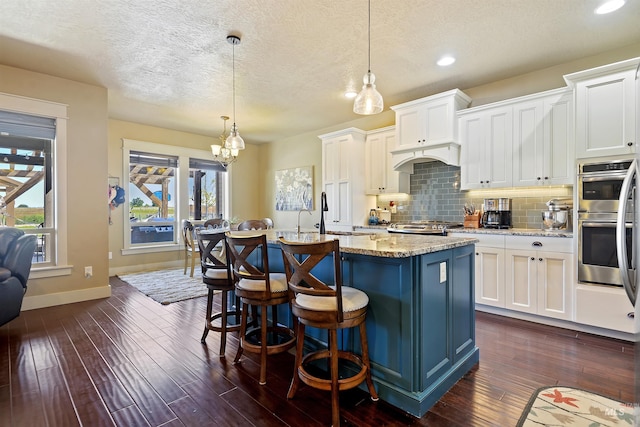 kitchen with a center island with sink, stainless steel double oven, backsplash, and dark wood-style flooring