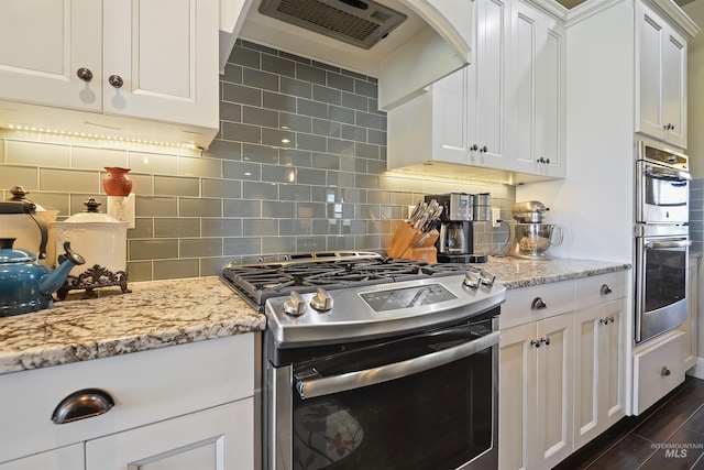 kitchen featuring tasteful backsplash, dark wood-type flooring, stainless steel appliances, wall chimney range hood, and white cabinetry