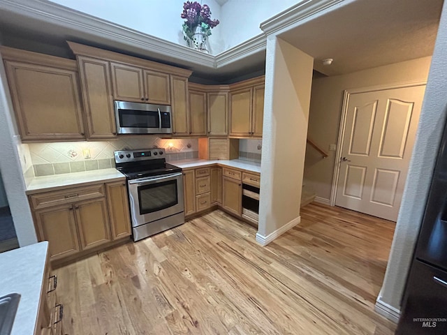 kitchen featuring stainless steel appliances, tasteful backsplash, light wood-type flooring, and ornamental molding