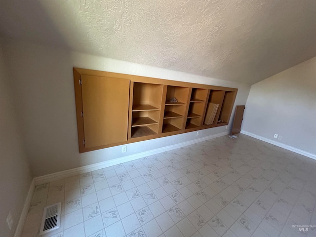 bonus room featuring built in features, a textured ceiling, and light tile patterned floors