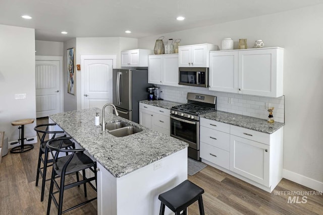 kitchen featuring stainless steel appliances, a sink, a kitchen breakfast bar, dark wood-style floors, and recessed lighting