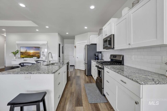 kitchen featuring appliances with stainless steel finishes, a sink, a center island with sink, white cabinets, and decorative backsplash