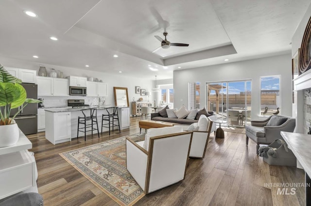 living area featuring a ceiling fan, a raised ceiling, dark wood-type flooring, and recessed lighting