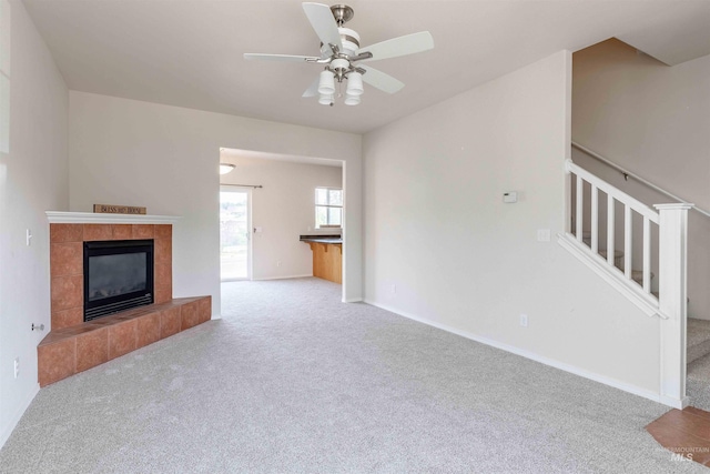 unfurnished living room with ceiling fan, light carpet, and a tile fireplace