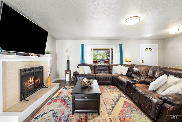 living room with a high end fireplace, a textured ceiling, baseboards, and wood finished floors