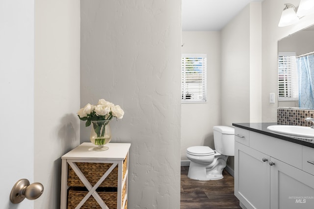 full bath with toilet, baseboards, wood finished floors, and vanity