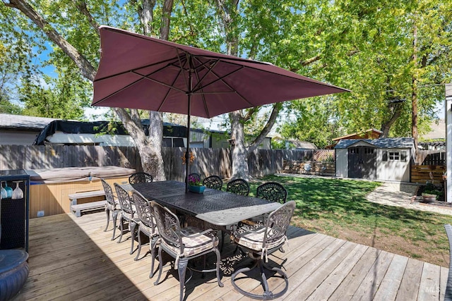wooden terrace with outdoor dining area, an outbuilding, a hot tub, a fenced backyard, and a storage unit
