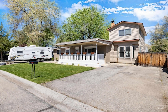 view of front of home with covered porch, a chimney, fence, aphalt driveway, and a front lawn