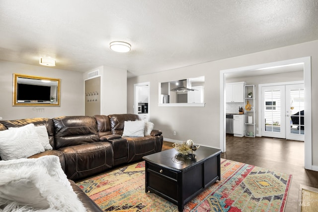 living room with wood finished floors, baseboards, a textured ceiling, and visible vents