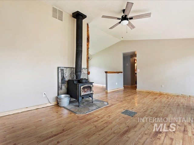 unfurnished living room with a ceiling fan, a wood stove, wood finished floors, and visible vents