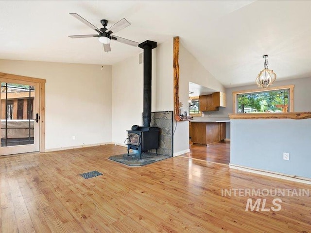 unfurnished living room featuring a ceiling fan, vaulted ceiling, a wood stove, light wood-type flooring, and baseboards