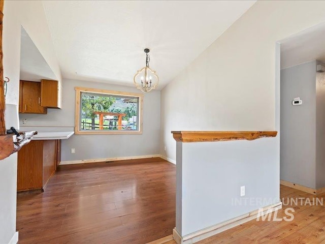 unfurnished dining area featuring baseboards, a notable chandelier, wood finished floors, and vaulted ceiling
