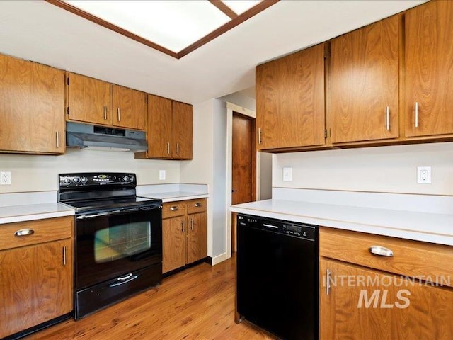 kitchen featuring brown cabinets, light countertops, light wood-type flooring, under cabinet range hood, and black appliances