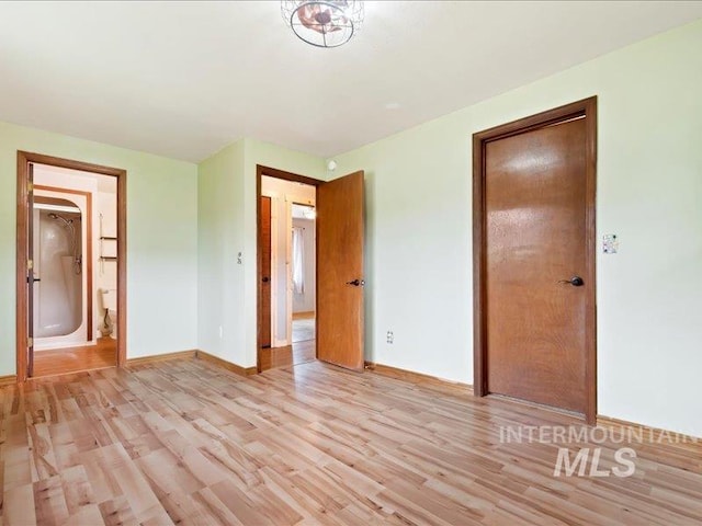 unfurnished bedroom featuring baseboards, ensuite bathroom, and light wood-style flooring