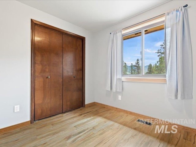 unfurnished bedroom featuring baseboards, a closet, light wood-type flooring, and visible vents