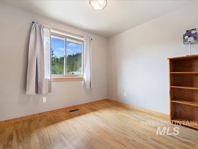 spare room with baseboards, wood finished floors, and visible vents