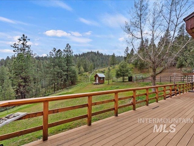 wooden terrace featuring fence, an outbuilding, a lawn, and a wooded view