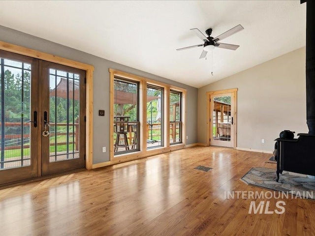 unfurnished living room featuring a wood stove, a wealth of natural light, baseboards, french doors, and vaulted ceiling