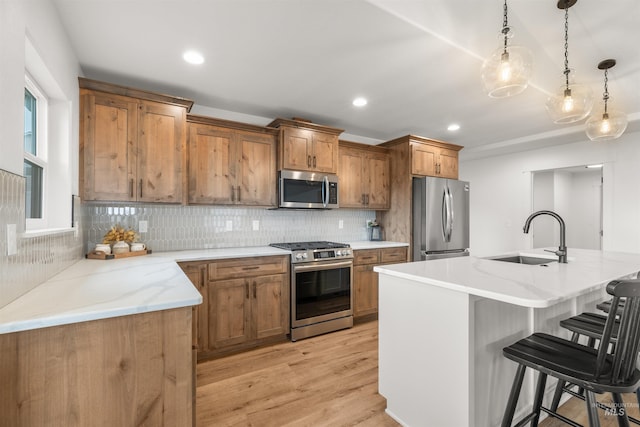 kitchen featuring appliances with stainless steel finishes, sink, a kitchen breakfast bar, decorative light fixtures, and a kitchen island with sink