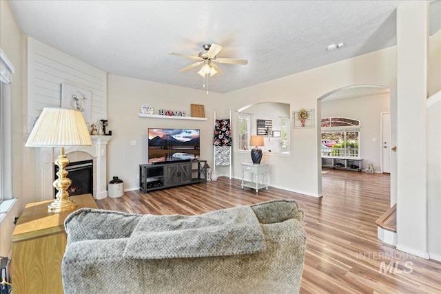 2175 W Willow Pointe Ave, Nampa, ID 83651 - living area with arched walkways, a ceiling fan, a glass covered fireplace, wood finished floors, and baseboards