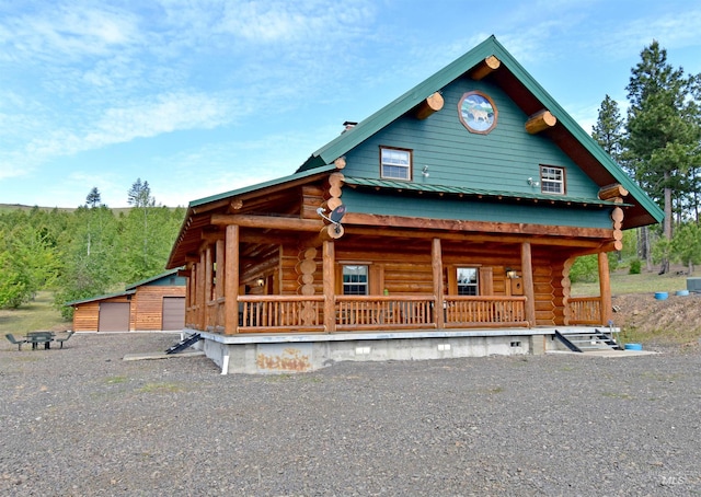 log-style house with covered porch, an outbuilding, and a garage