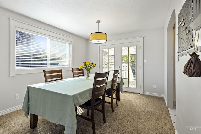 dining space featuring a healthy amount of sunlight, french doors, light colored carpet, and baseboards