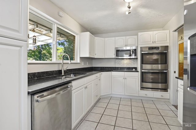 kitchen with a sink, appliances with stainless steel finishes, white cabinets, and light tile patterned floors