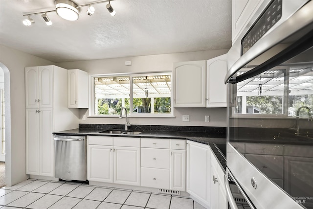 kitchen featuring dark countertops, appliances with stainless steel finishes, arched walkways, white cabinetry, and a sink